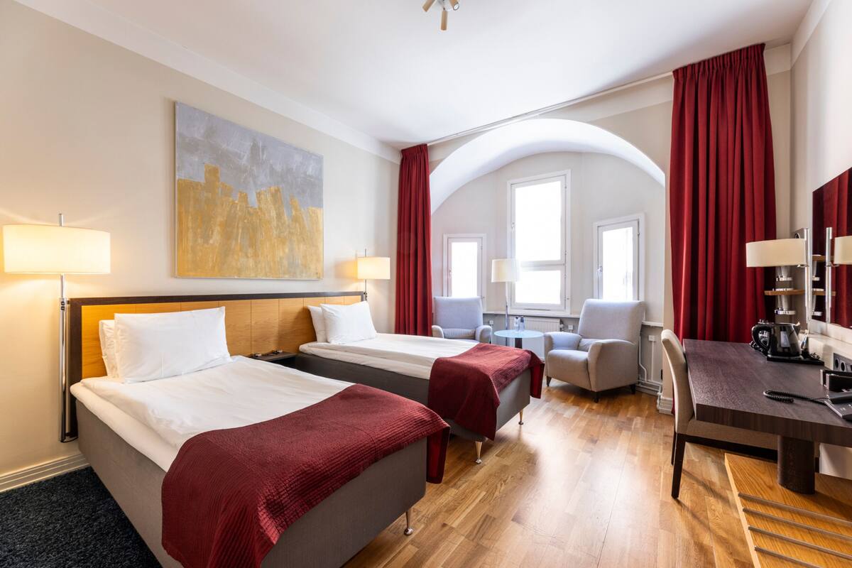A hotel room with two beds, a desk, a chair, and a large window.