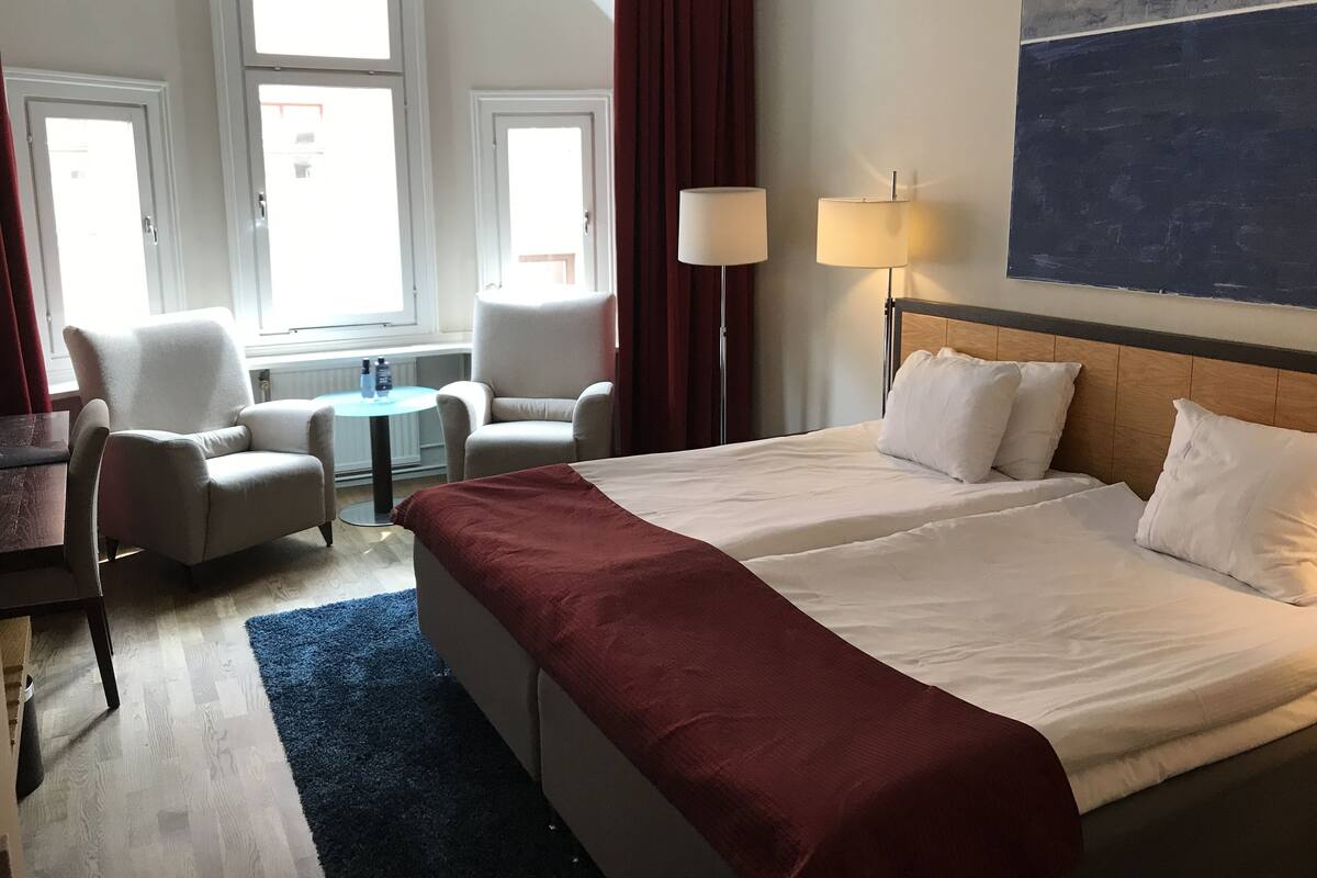 A hotel room with a large bed, two armchairs, a small table, and two lamps.