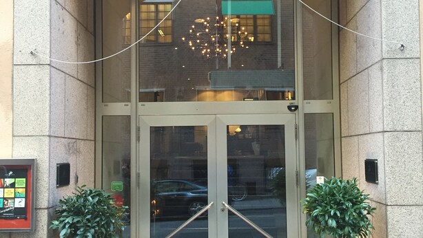 A hotel entrance with a glass door, a red mat, and two potted plants. - ProfilHotels Riddargatan (Stockholm)