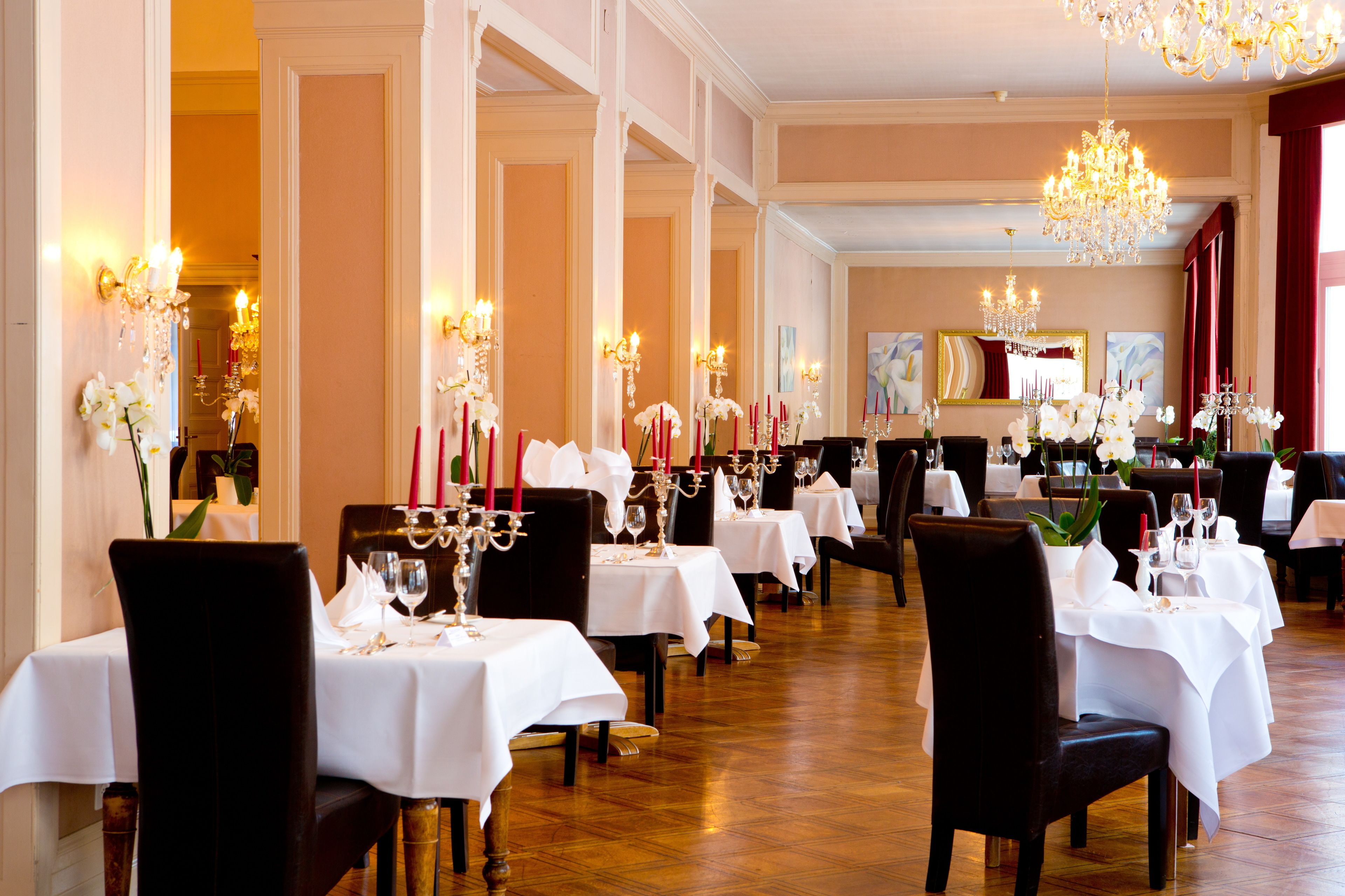A formal dining room with multiple tables, each set with white tablecloths, candles, and floral arrangements.