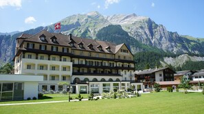 Un hotel de estilo arquitectónico europeo tradicional, con múltiples balcones y un paisaje montañoso de fondo.