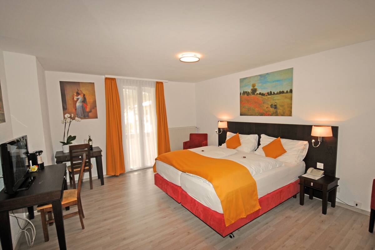 Ein Hotelzimmer mit Bett, Nachttischen, einem Schreibtisch mit Stuhl, einem Fernseher und Kunstwerken an den Wänden.