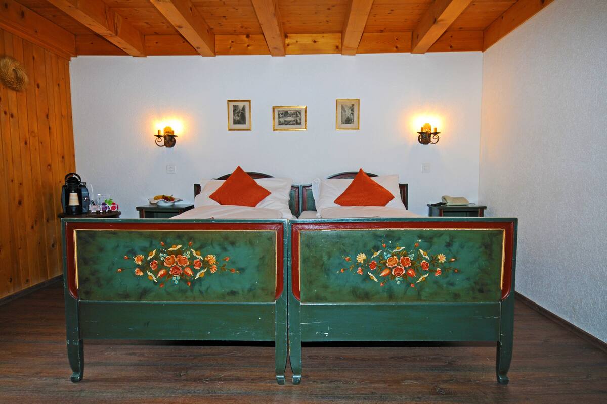 Ein Zimmer mit zwei mit grünem Stoff bezogenen Betten mit floralen Mustern, einer Holzzielung und an der Wand befestigten Leuchten.