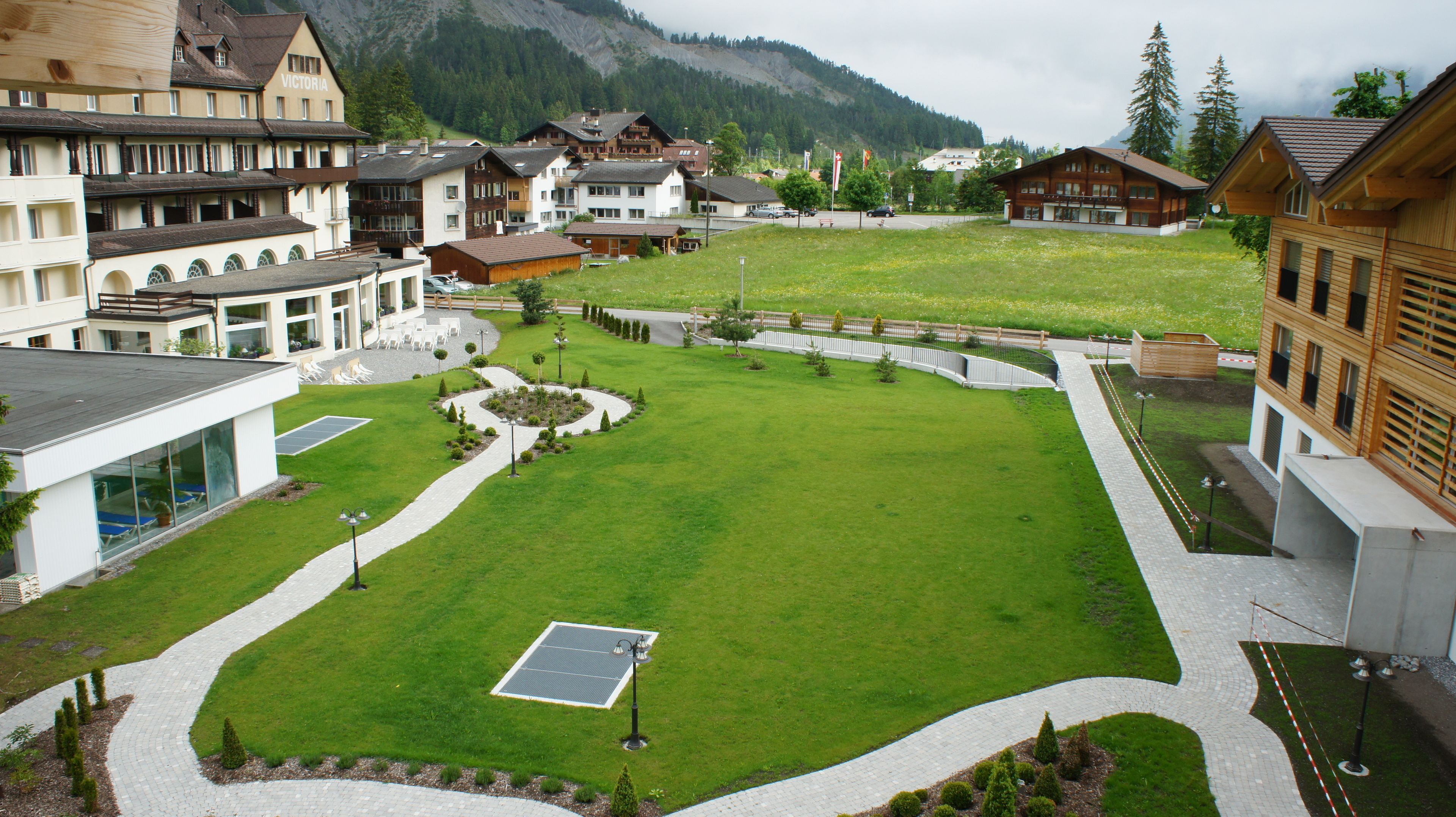 A hotel courtyard with a solar panel, paved walkways, and a variety of buildings including a restaurant and a hotel with multiple floors.