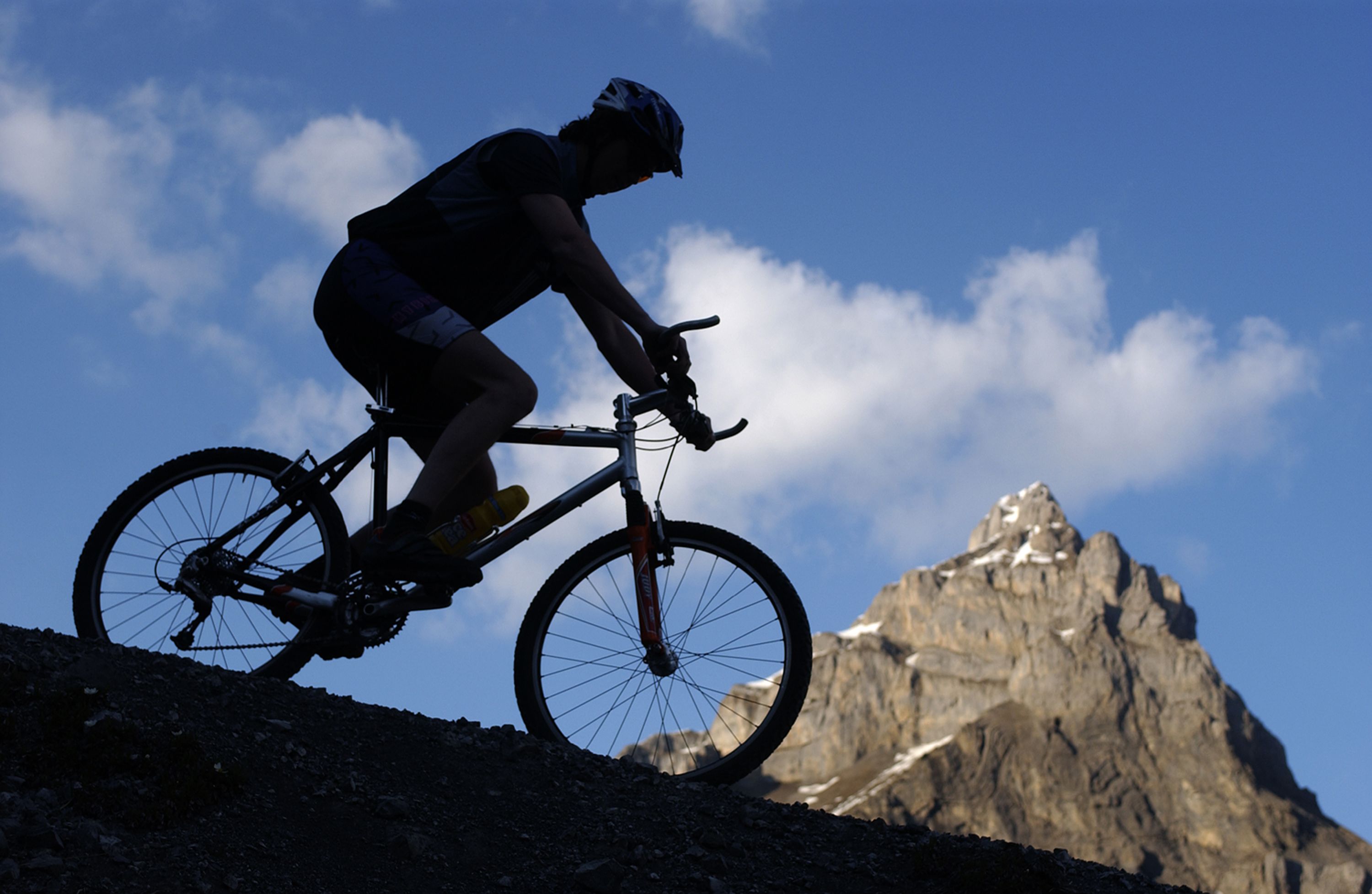 A mountain biker on a trail with a mountain in the background.
