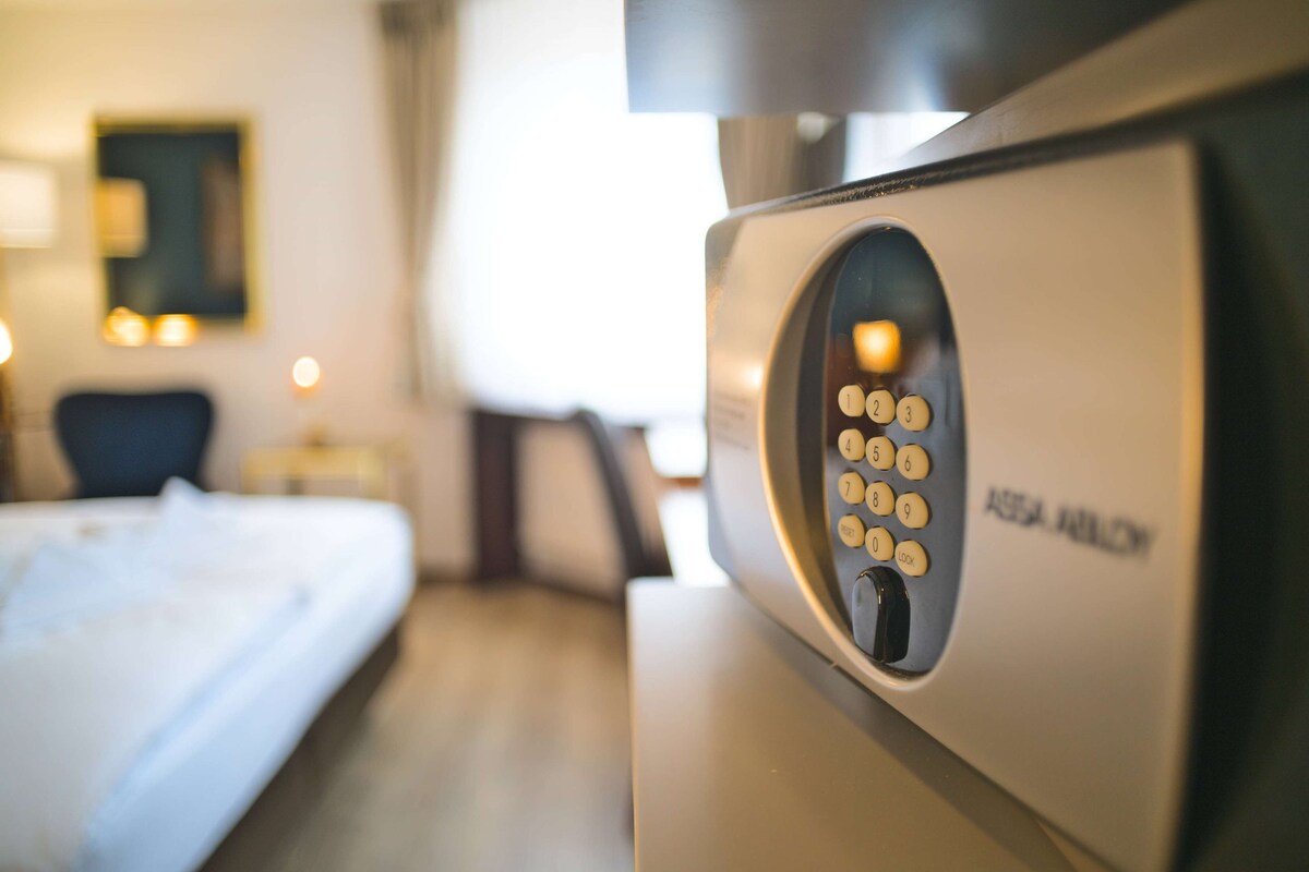 A hotel room with a bed, a desk, and a wall-mounted control panel.