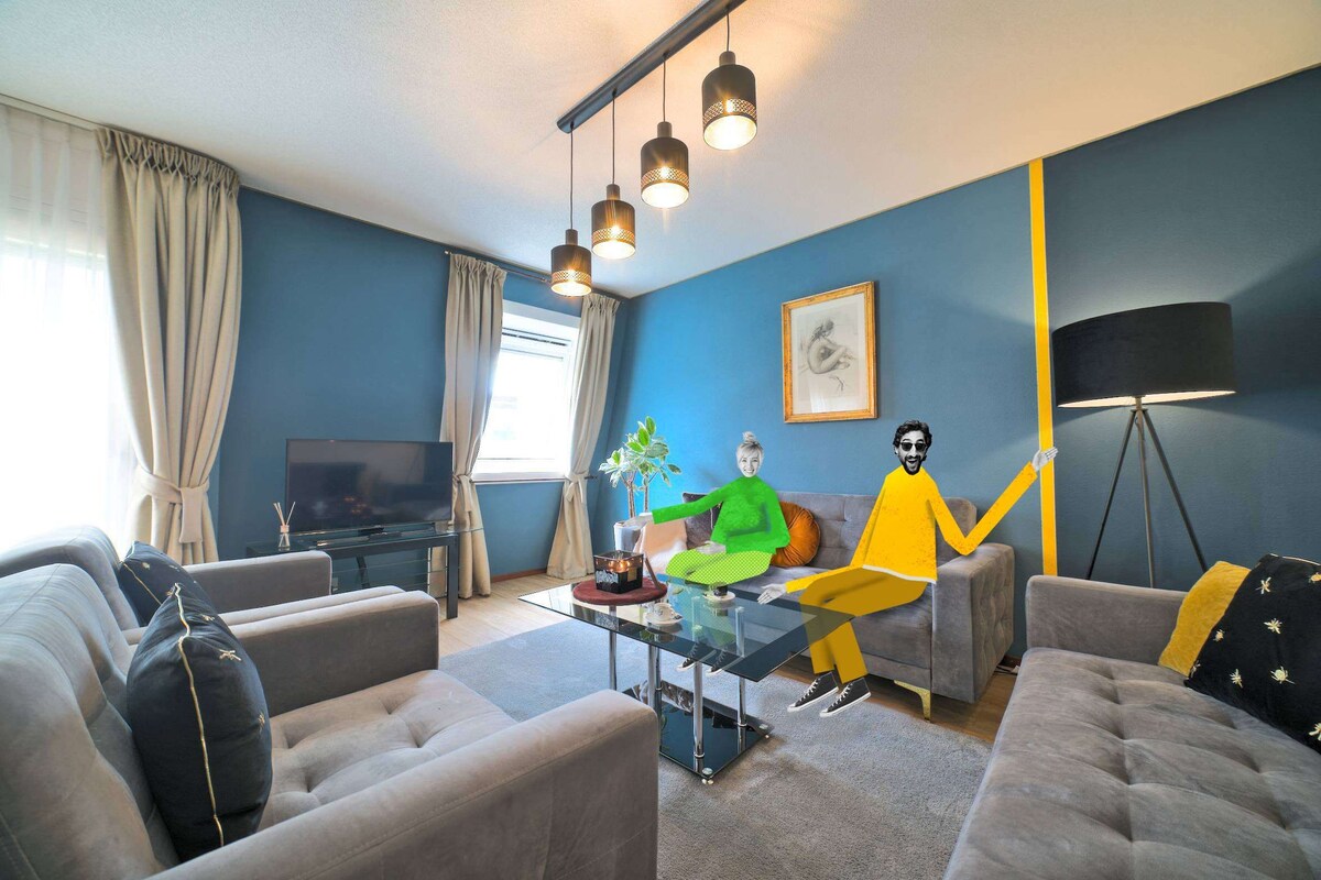A modern living room with a flat-screen TV, a coffee table, sofas, and a floor lamp.