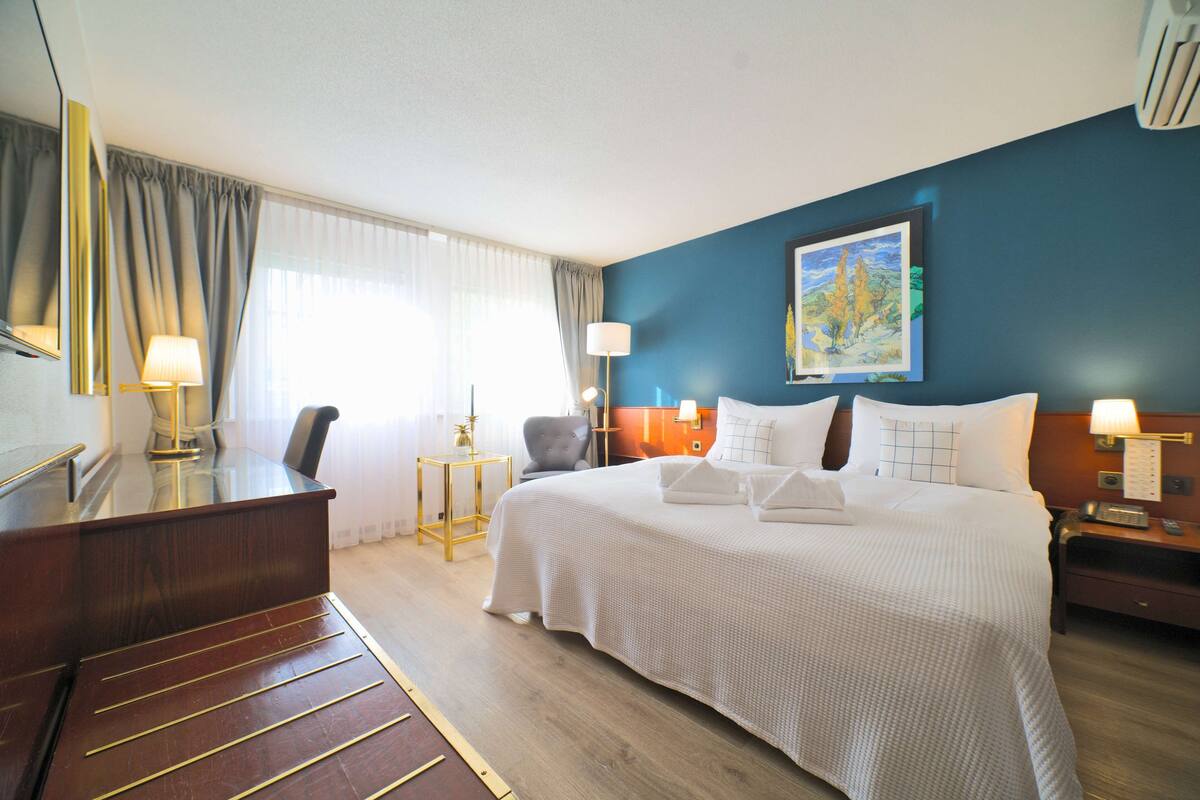 Ein Hotelzimmer mit einem großen Bett, einem Schreibtisch, einem Stuhl und einem Nachttisch mit einer Lampe.