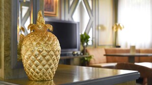 Una habitación con un jarrón dorado decorativo sobre una mesa, una televisión y un sofá al fondo.