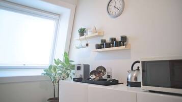 Una cocina con armarios blancos, un microondas, un hervidor y un reloj en la pared.
