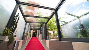 Un pasillo con alfombra roja, paredes de vidrio y plantas en macetas.