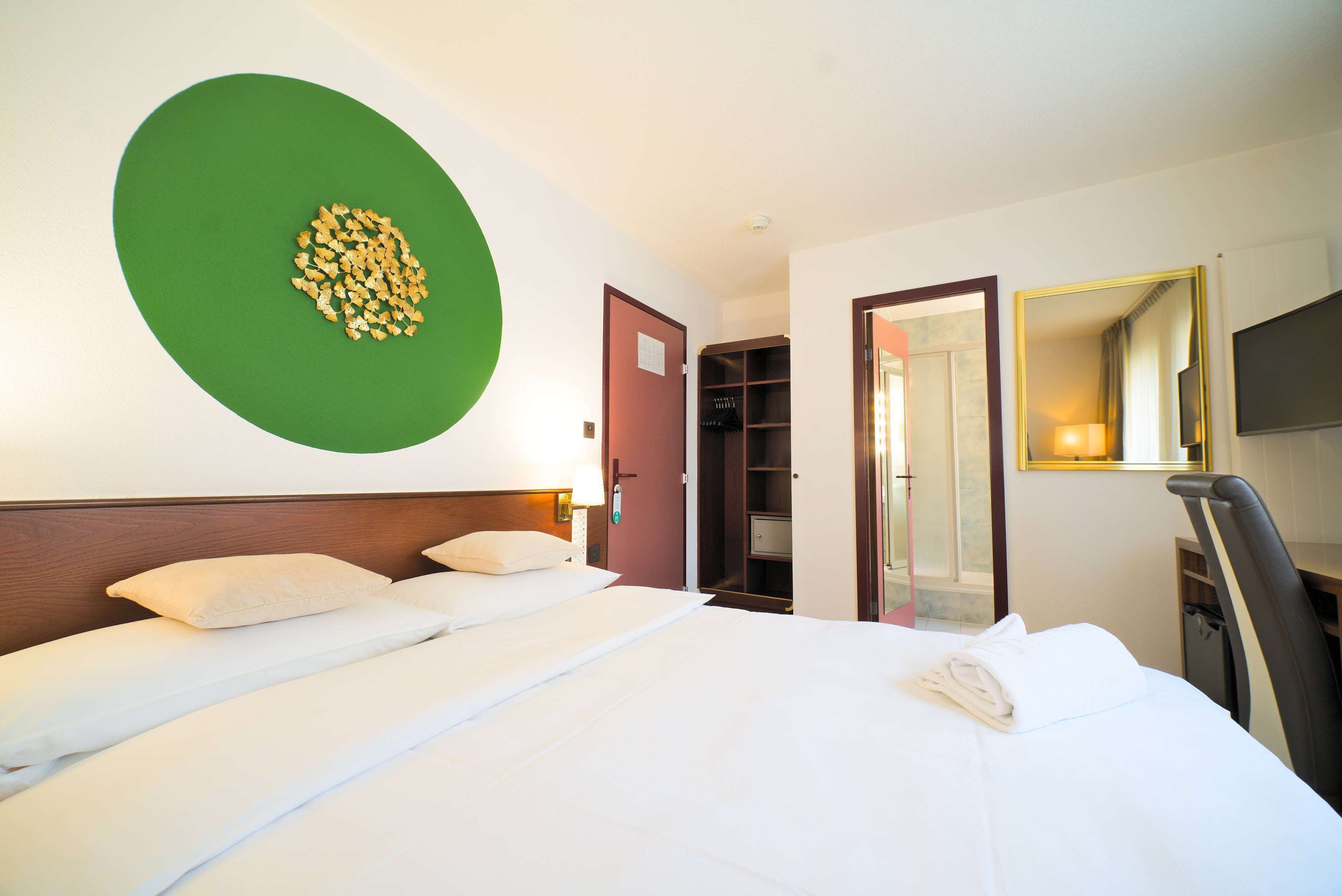 A hotel room with a large bed, a green wall decoration, a wardrobe, and a mirror.