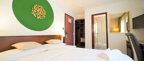 A hotel room with a large bed, a green wall decoration, a wardrobe, and a mirror.