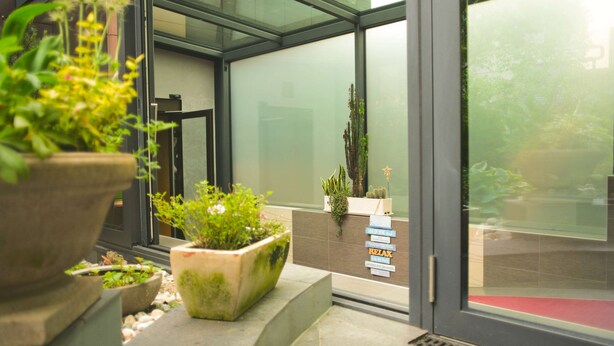 Una entrada moderna a un edificio con plantas en macetas y una puerta de cristal.
