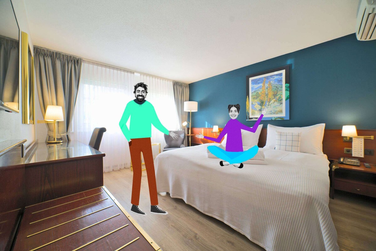 A hotel room with a bed, a desk, a chair, a lamp, and a painting on the wall.