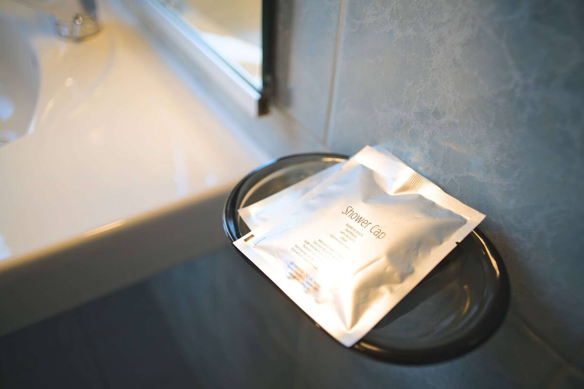 Ein Badezimmer mit einem weißen Waschbecken und einer Duschhaube auf einer Glasablage.
