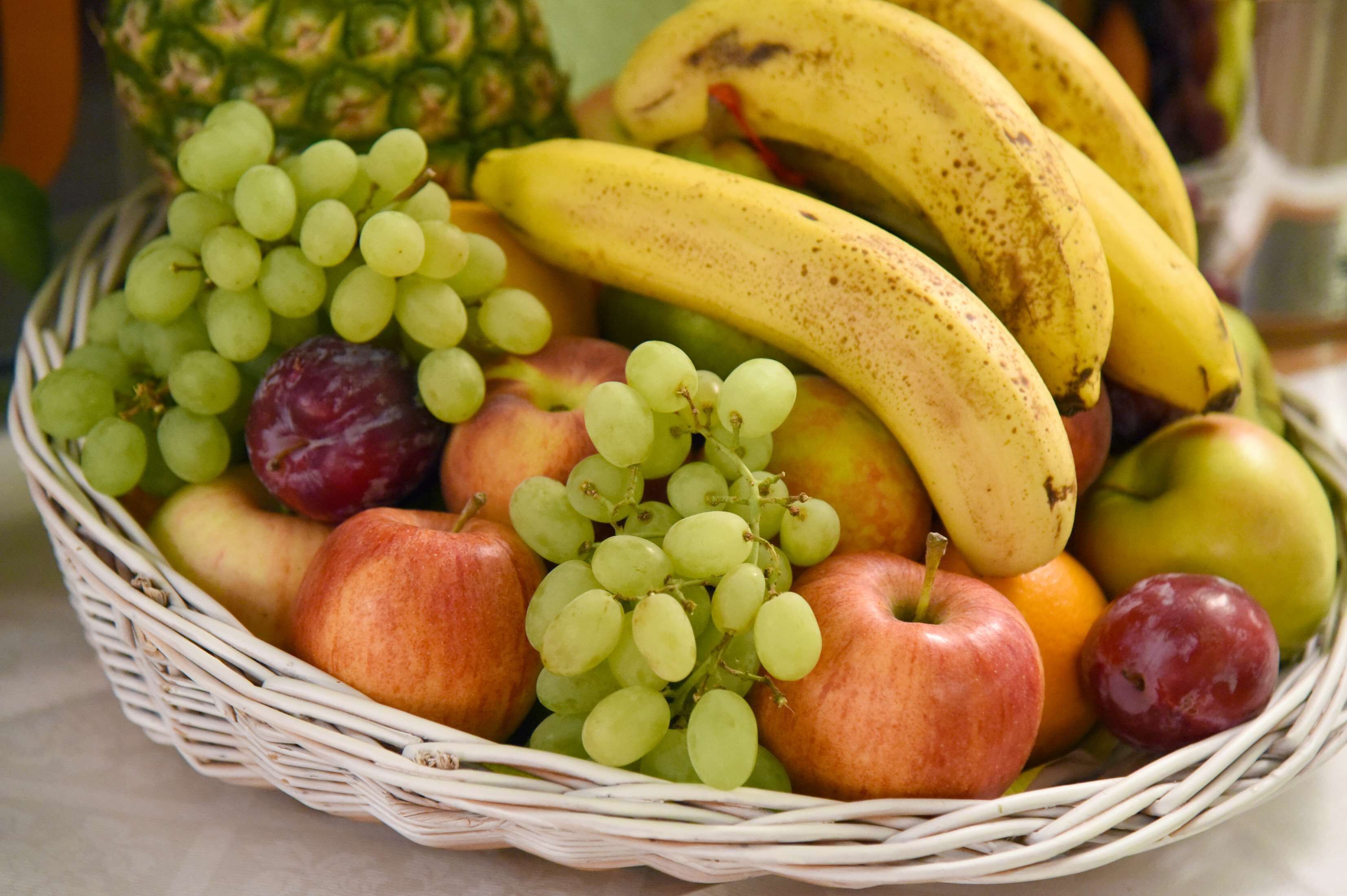 A wicker basket filled with various fruits including bananas, grapes, apples, and a pineapple.