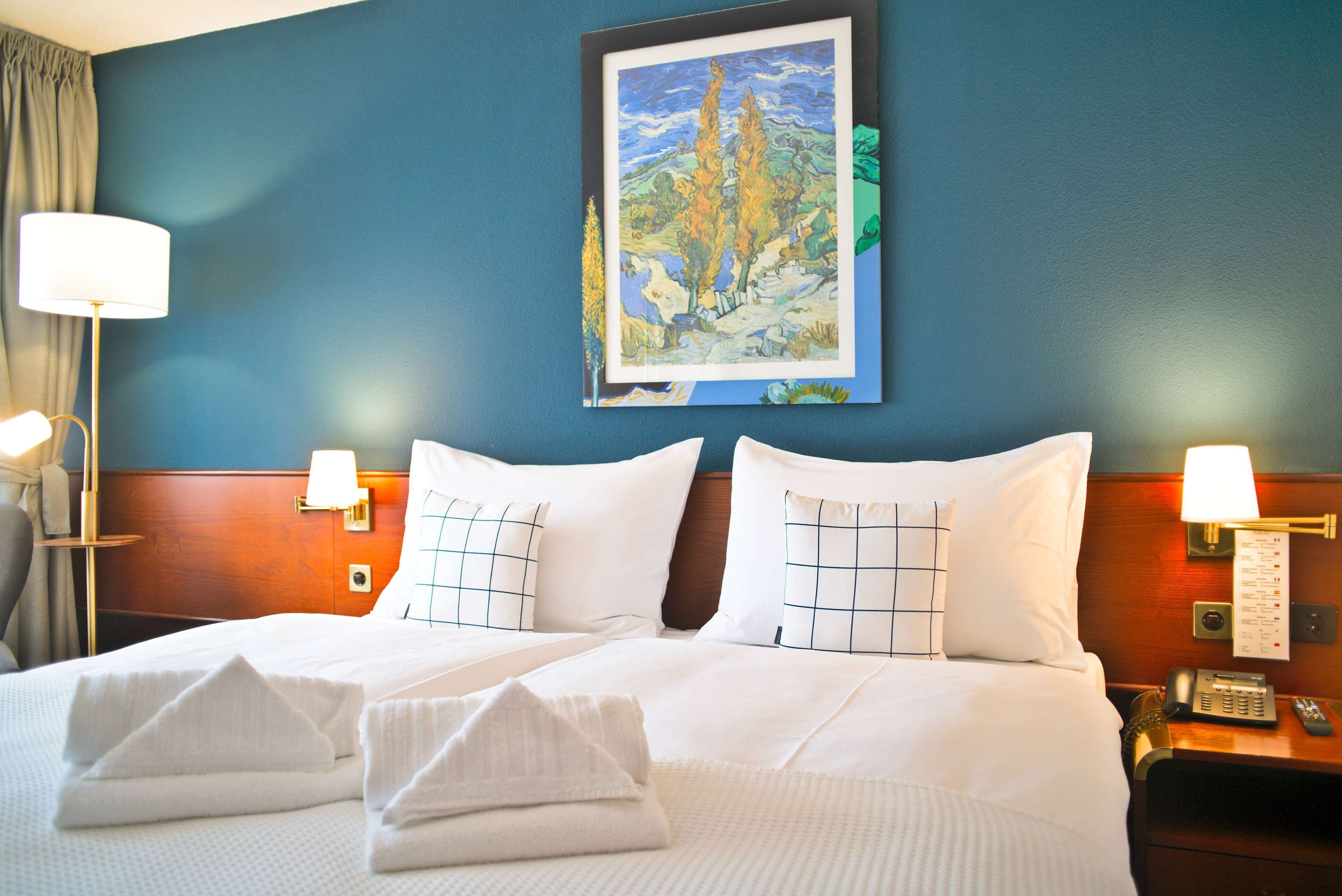 Habitación de hotel con una cama grande, dos lámparas de noche, un cuadro en la pared y una mesita de noche con un teléfono.