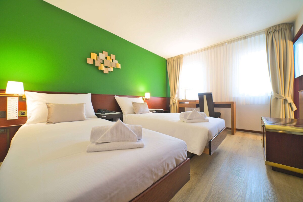 A hotel room with two beds, a desk, and a chair.