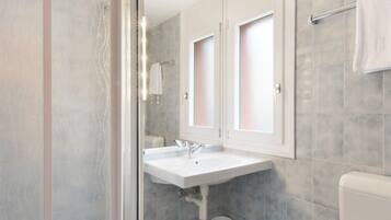 Un baño moderno con cabina de ducha de vidrio, un lavabo blanco y un inodoro.