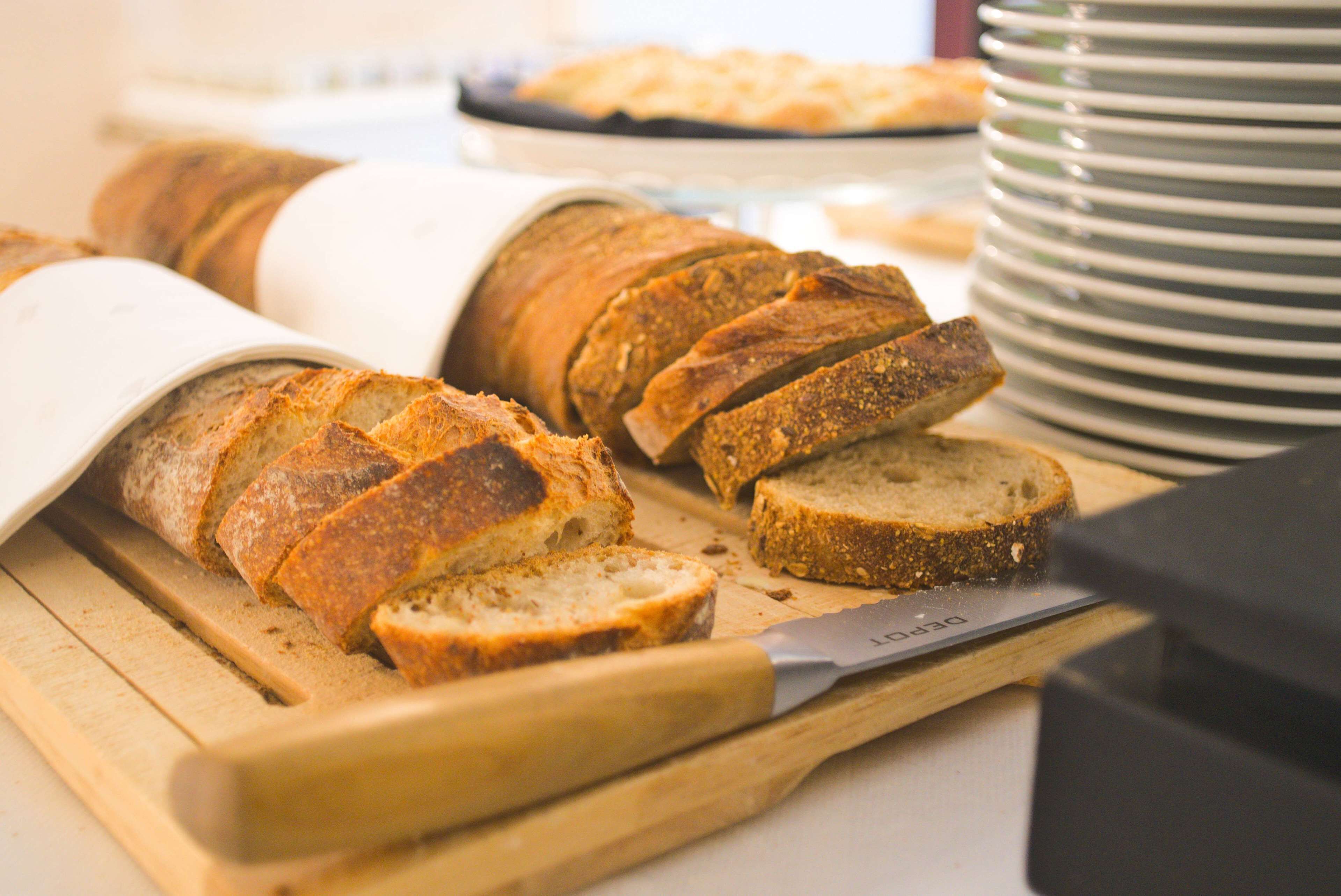 Des tranches de pain sur une planche à découper, avec un couteau à côté, une pile d’assiettes et un arrière-plan flou.
