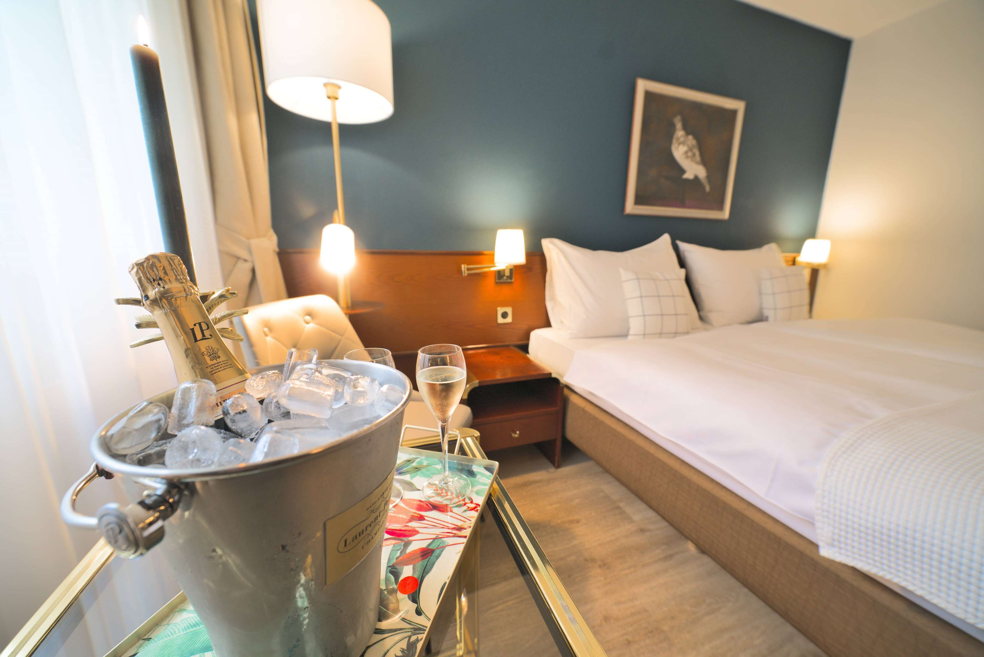 A hotel room with a bed, bedside lamps, a nightstand, a bucket of ice, and a glass of champagne.