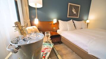 A hotel room with a bed, bedside lamps, a nightstand, a bucket of ice, and a glass of champagne.