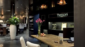A modern interior with a wooden table, white chairs, a potted plant, and a Thesoni sign. - Boutiquehotel Thessoni Classic Zürich (Regensdorf)
