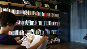 A person reading a magazine in a room with a bookshelf filled with books. - Boutiquehotel Thessoni Classic Zürich (Regensdorf)