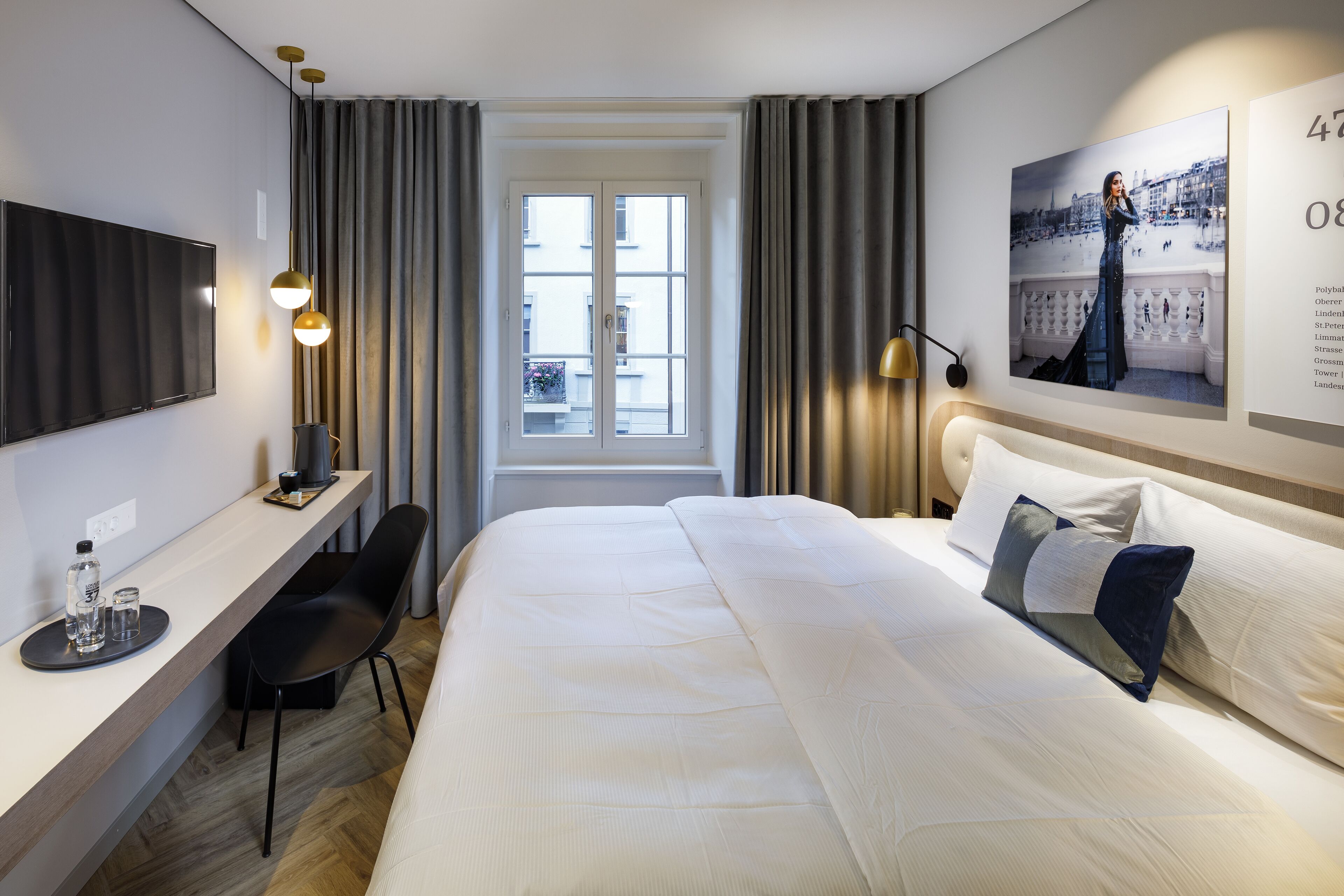 Habitación de hotel con una cama grande, un escritorio con silla, televisión y ventana con cortinas.