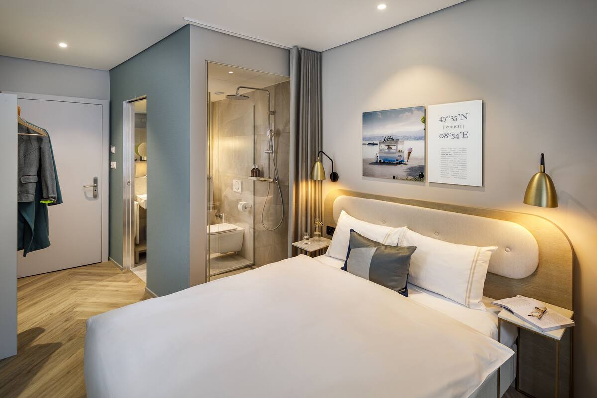 Moderni hotellihuone, jossa on suuri sänky, suihkutila ja näkymä kaupunkiin.