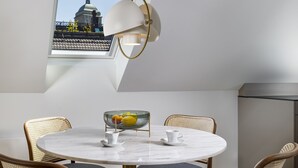 Un espace repas moderne avec une table ronde, quatre chaises, un saladier de fruits et une fenêtre donnant sur un immeuble.