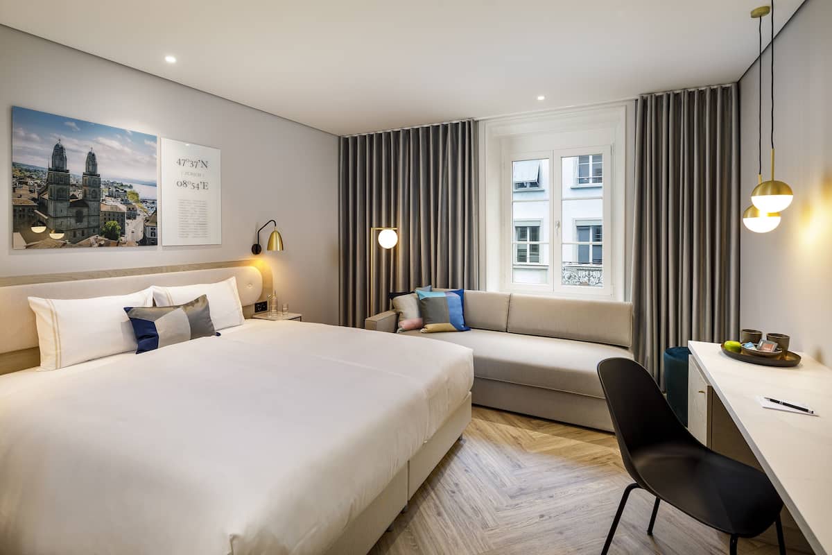 Hotellihuone, jossa on suuri sänky, sohva, työpöytä ja ikkuna, jossa on verhot.