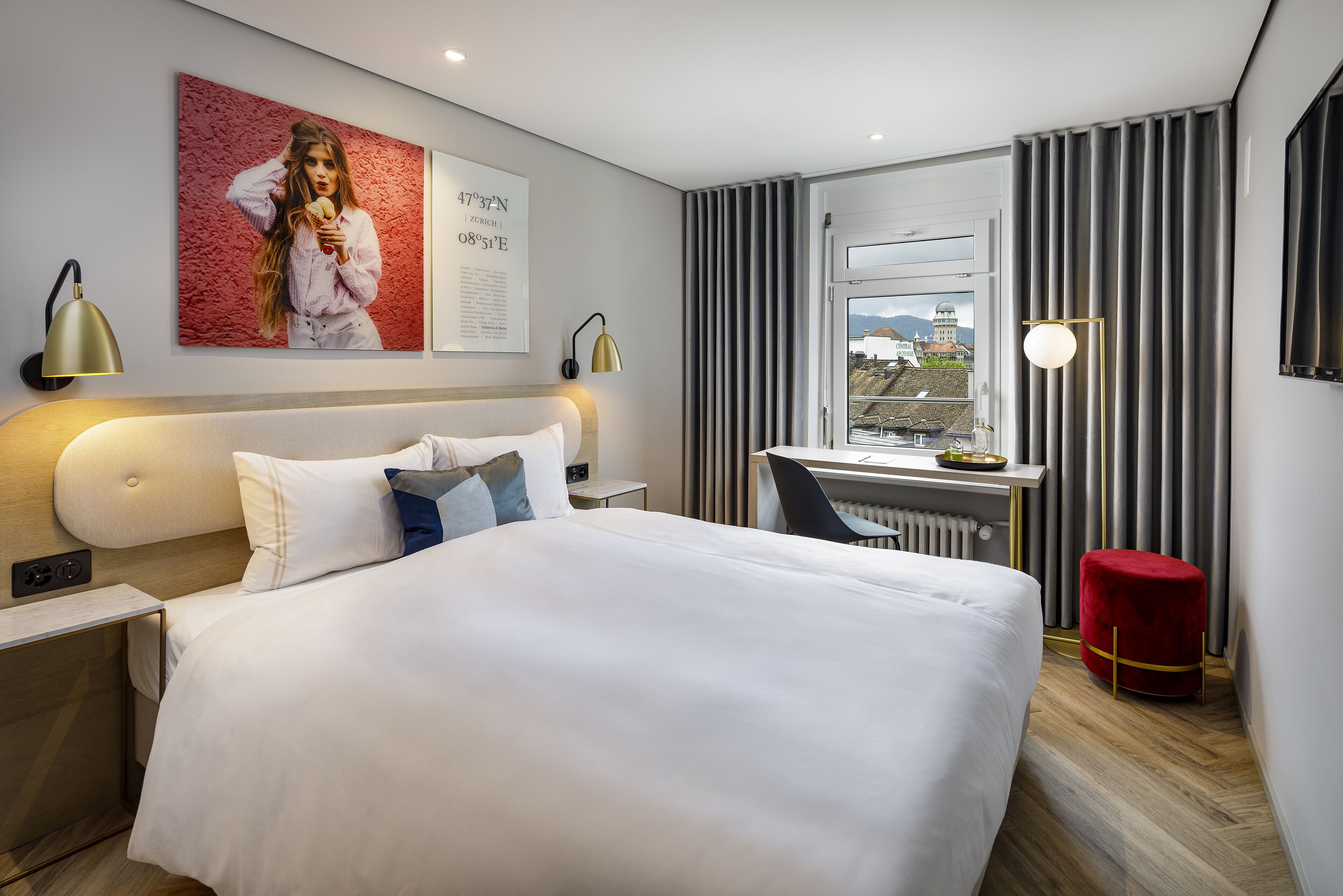 A modern hotel room with a large bed, a desk, and a view of the city.
