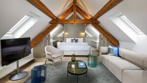 Une chambre de style loft moderne avec un plafond en pente, des fenêtres de toit, un grand lit, un canapé, une table basse et un téléviseur.