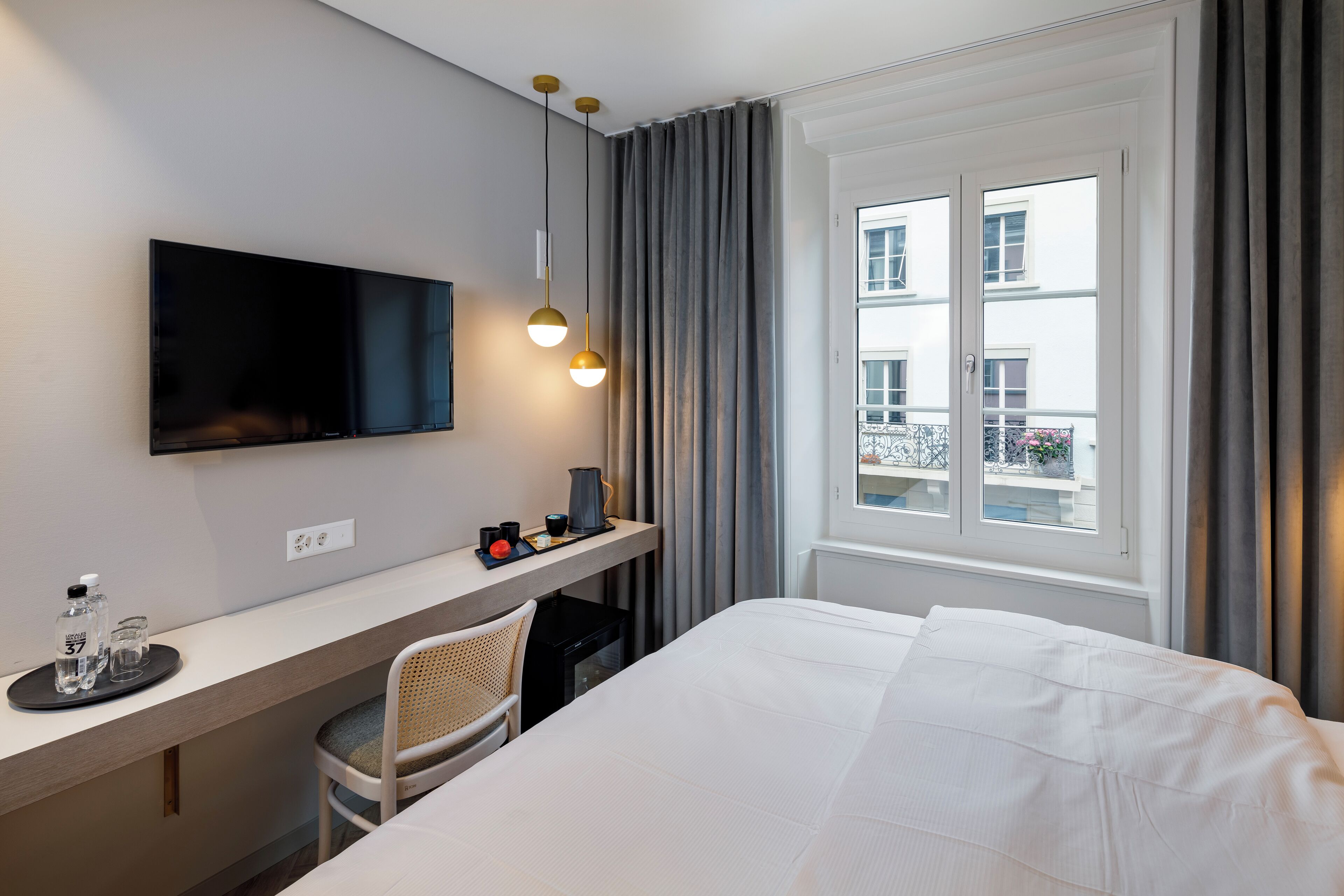 Ein Hotelzimmer mit einem Bett, einem Schreibtisch mit Fernseher, einem Sessel und einem Fenster mit Vorhängen.
