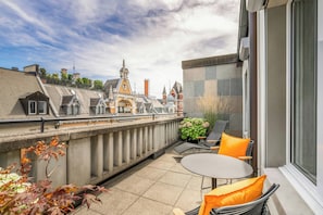 Une terrasse sur le toit, avec une table et des chaises, offrant une vue sur des bâtiments historiques et un ciel dégagé.