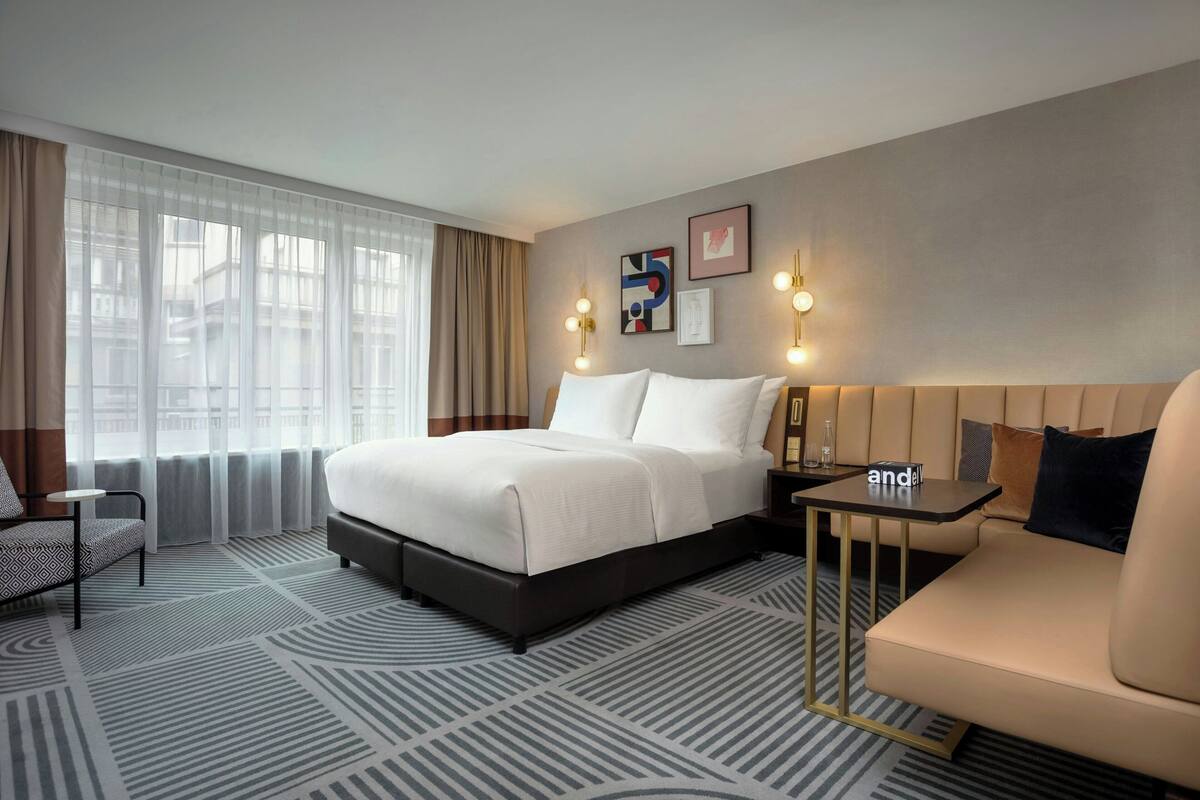 Une chambre d’hôtel avec un lit, un canapé, une petite table et une fenêtre avec des rideaux.