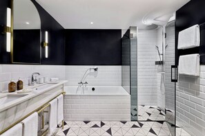 A modern bathroom with a white bathtub, a glass-enclosed shower, and a black and white tiled floor. - Neues Schloss Privat Hotel Zurich, Autograph Collection (Zürich)