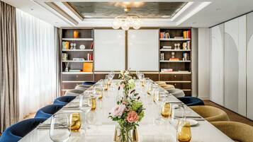 A long dining table set for a formal meal with a floral centerpiece, surrounded by bookshelves and a modern chandelier.