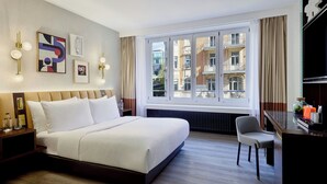 Een moderne hotelkamer met een groot bed, een bureau en uitzicht op de stad door middel van ramen van de vloer tot aan het plafond.