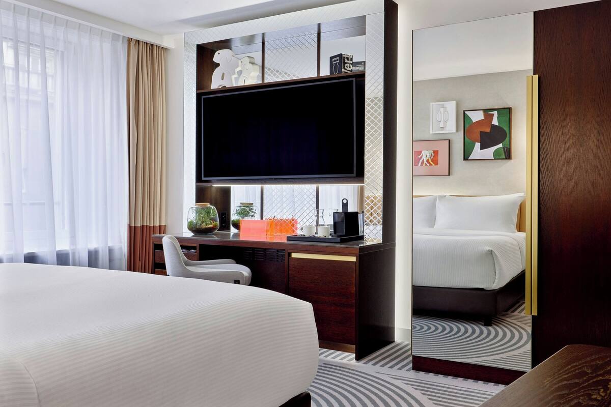 Une chambre d’hôtel avec un grand lit, un bureau doté d’un téléviseur à écran plat, une chaise et une petite table sur laquelle est posée une plante.