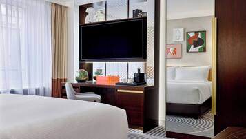 Quarto de hotel com uma cama grande, uma escrivaninha com televisão de tela plana, uma cadeira e uma mesinha com uma planta.