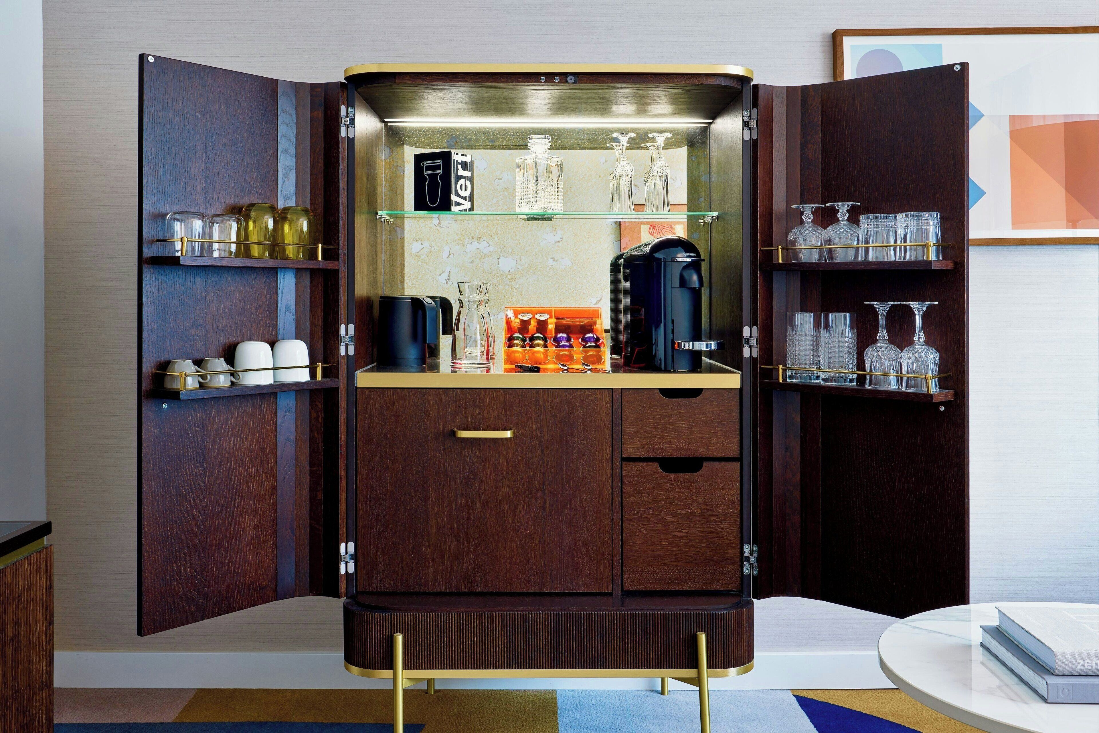 Eine kompakte Minibar mit dunklem Holzrahmen, Glasbögen, einer Kaffeemaschine und verschiedenen Gläsern.