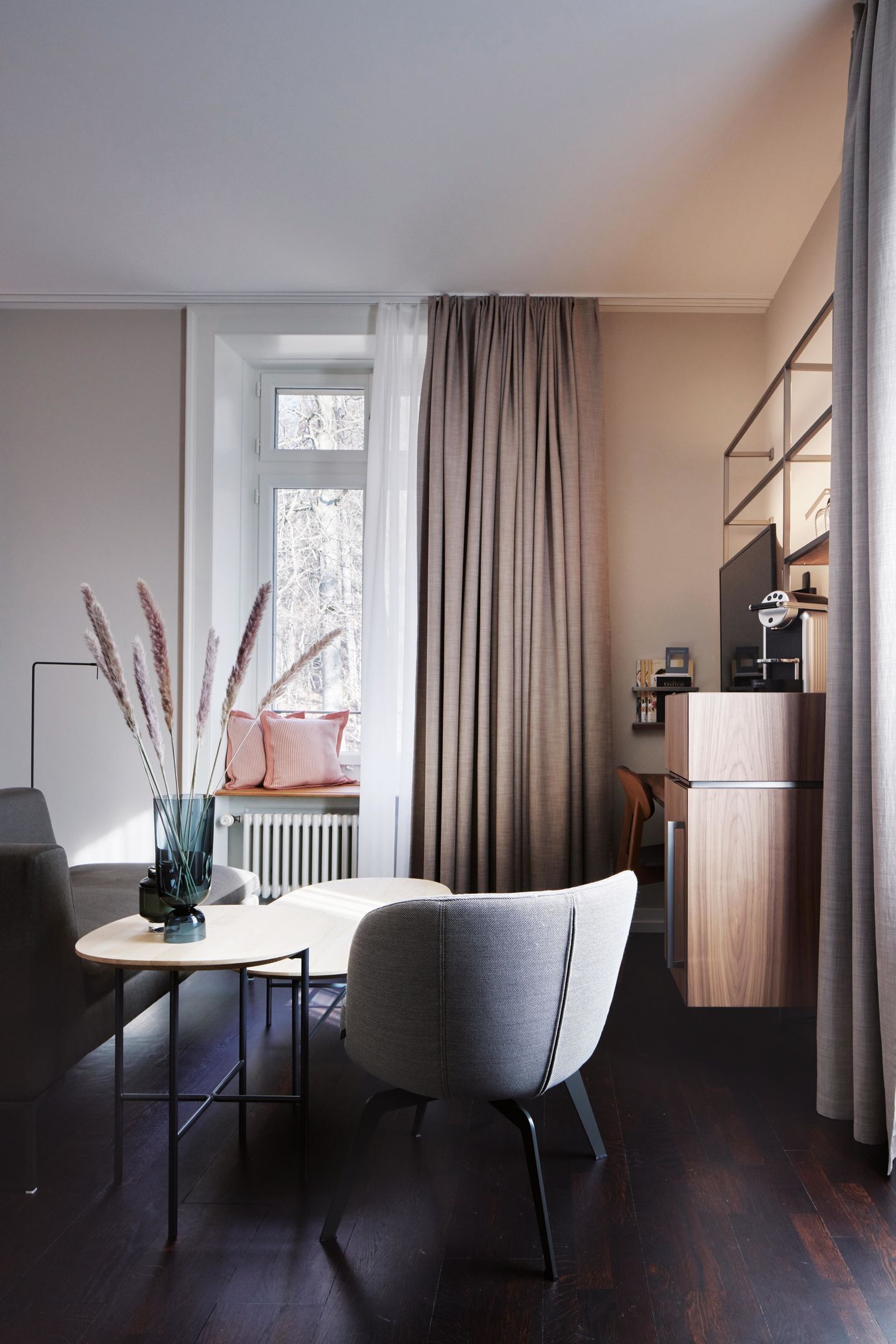 A modern room with a wooden desk, a chair, a radiator, a window with curtains, and a bookshelf.