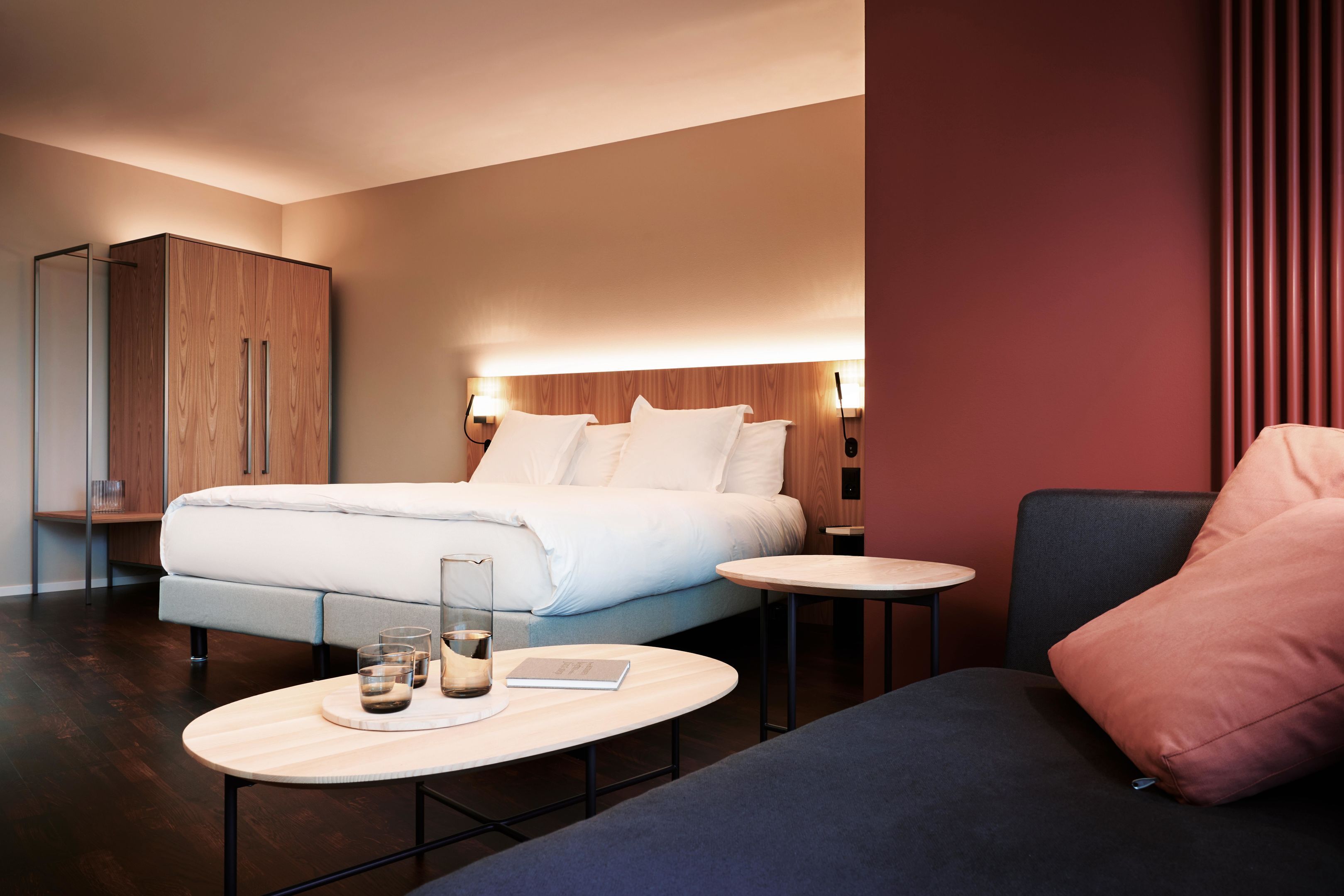 A modern hotel room with a bed, bedside tables, a sofa, and a wardrobe.