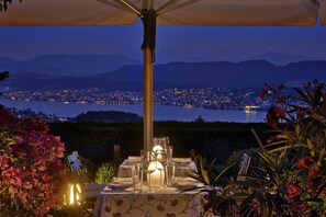 An outdoor dining setup with a table set for two, overlooking a cityscape and a body of water at dusk.