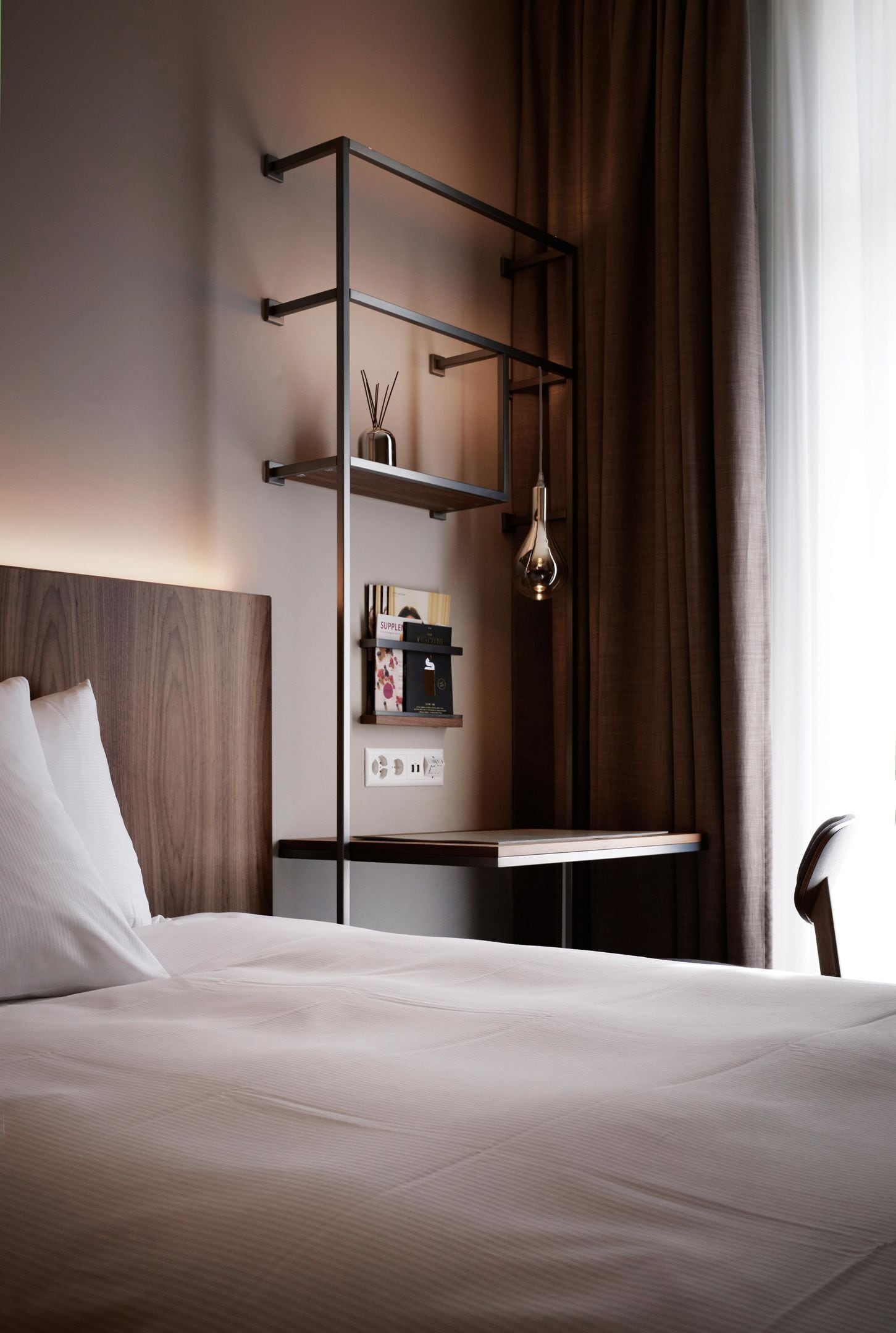 Ein modernes Hotelzimmer mit einem Bett, einer Wandablage mit Dekoration und einer hängenden Leuchte.