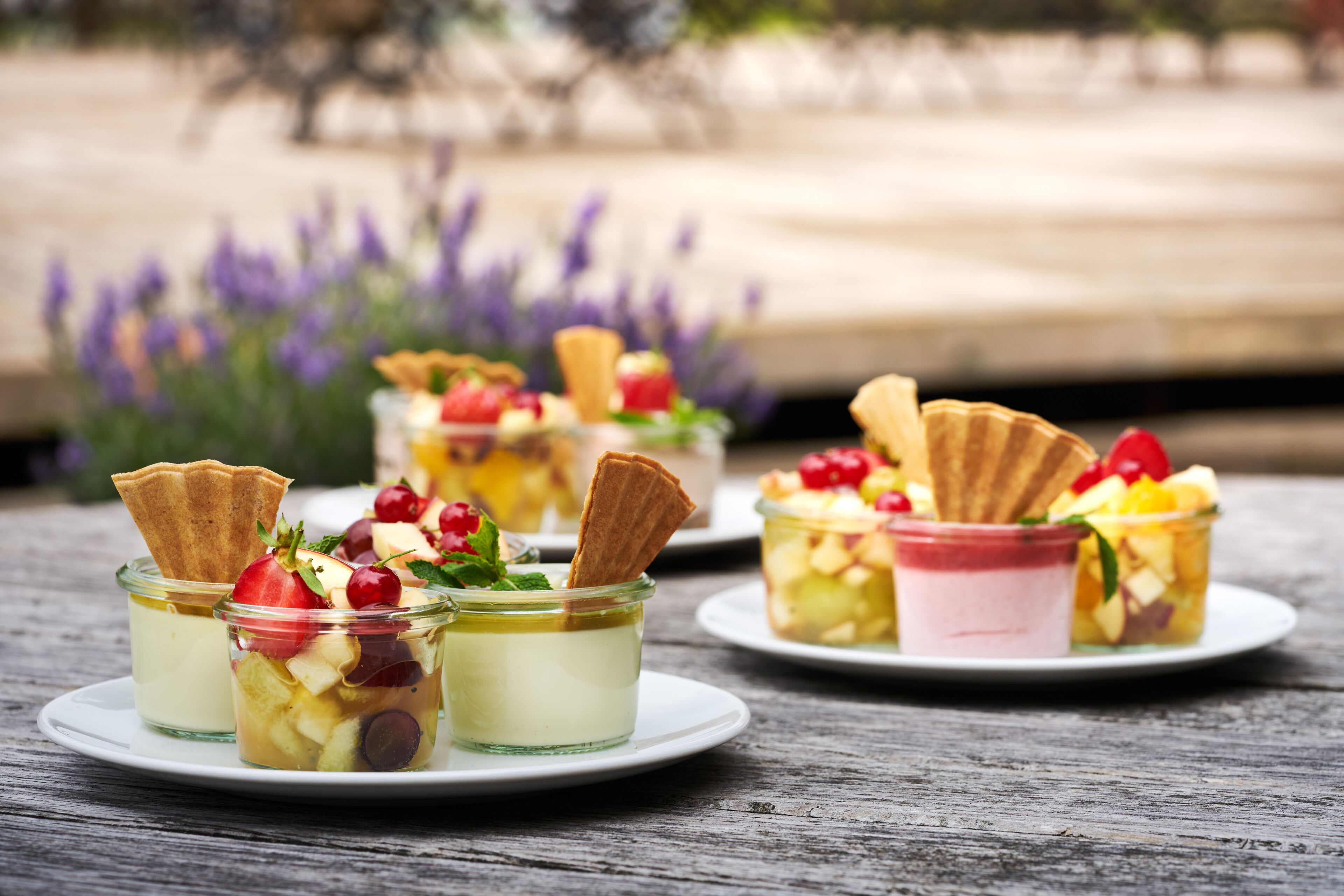 Tres copas de postre sobre una mesa de madera, con un fondo borroso de flores moradas.