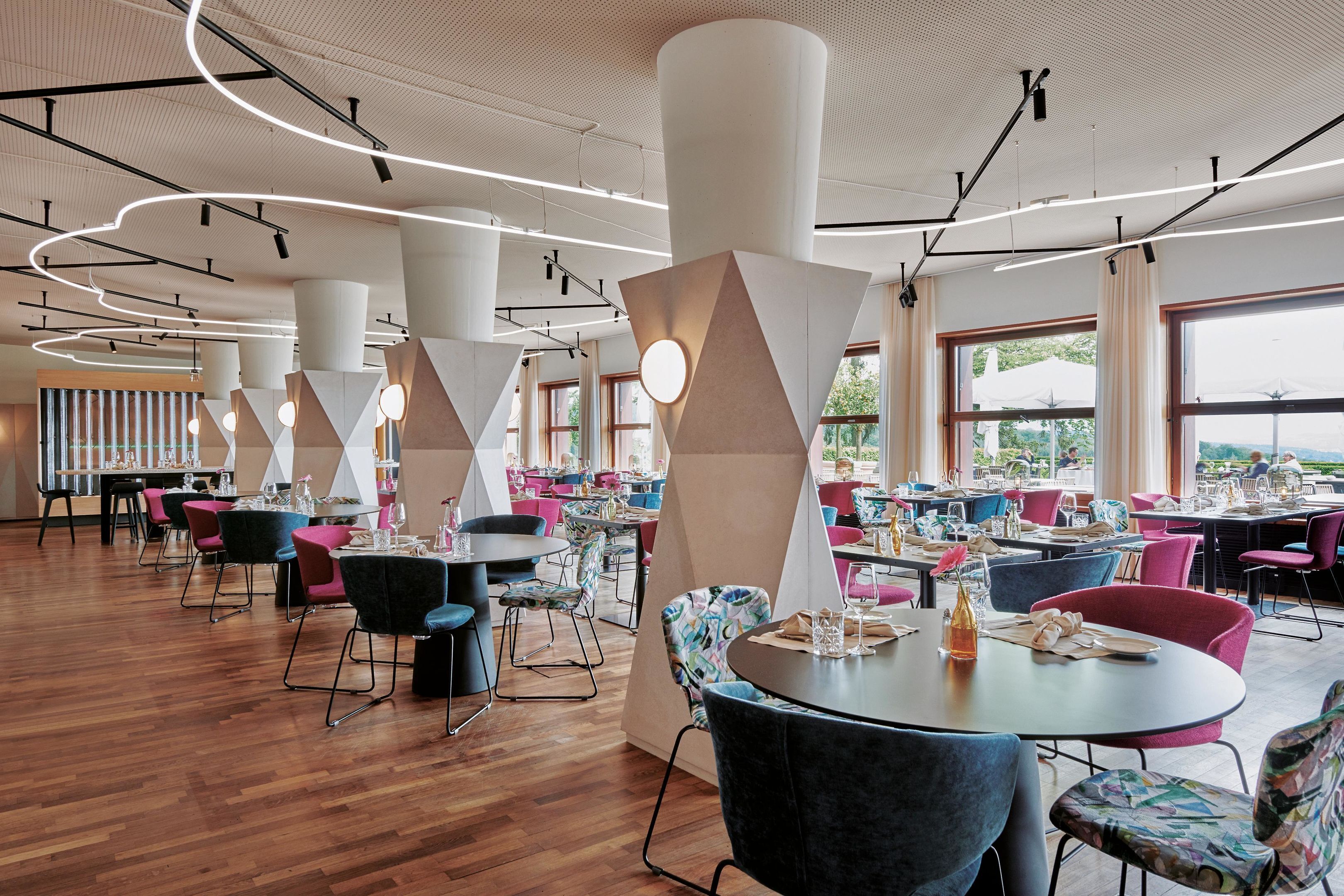 Ein modernes Restaurant mit runden Tischen, bunten Stühlen und Blick ins Freie.